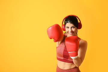 Sporty female boxer with headphones on color background