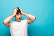 © LIGHTFIELD STUDIOS - shocked young man looking away while holding hands on head on blue background