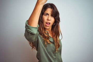 Wall Mural - Young beautiful woman wearing green shirt standing over grey isolated background angry and mad raising fist frustrated and furious while shouting with anger. Rage and aggressive concept.