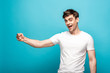 © LIGHTFIELD STUDIOS - cheerful man showing fist while looking at camera on blue background