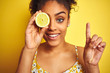© Krakenimages.com - Young african american woman holding slice of lemon over isolated yellow background surprised with an idea or question pointing finger with happy face, number one
