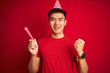 © Krakenimages.com - Asian chinese man on birthday celebration wearing funny hat over isolated red background screaming proud and celebrating victory and success very excited, cheering emotion
