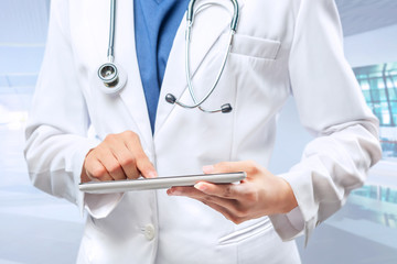 Woman doctor in white lab coat and stethoscope using tablet