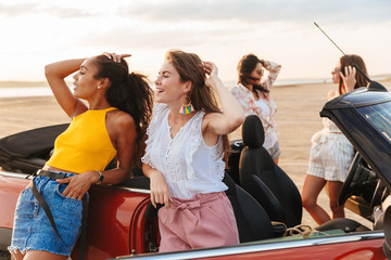 Poster - Happy young pretty women friends standing near car at the beach.