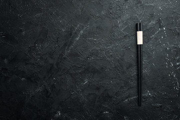 Wall Mural - Wooden chopsticks on a black stone background. Top view. Free space for your text.