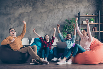 Wall Mural - Nice attractive cheerful glad confident guy company specialist development manager employee sitting on bag chairs rising hands up attainment at industrial wooden loft interior workplace workstation