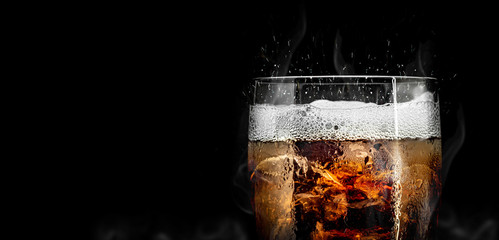 Soft drink glass with ice splash on cool smoke background. Cola glass with summer refreshment.