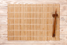 Two Sushi Chopsticks With Empty Brown Bamboo Mat Or Wood Plate On Brown Wooden Background Top View With Copy Space. Empty Asian Food Background