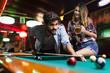© NDABCREATIVITY - Young couple playing snooker together in bar
