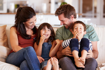 Wall Mural - Mid adult white couple and their two young children sitting on a sofa at home smiling at each other