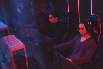 Wall Mural - Group of concentrated e-sport gamer sitting in gaming chairs and using modern powerful computers in club