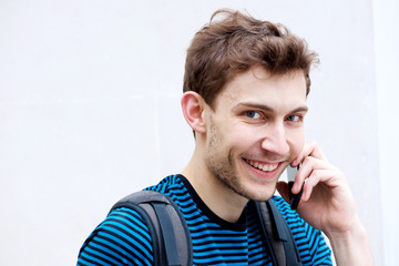 Wall Mural - Close up young man smiling while talking with cellphone by white background