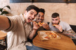 © Drobot Dean - Three cheerful men eating pizza at the cafe table