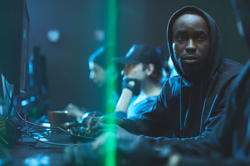 Wall Mural - Tired young Black app developer in hoodie sitting at table and advising colleague while working on new app