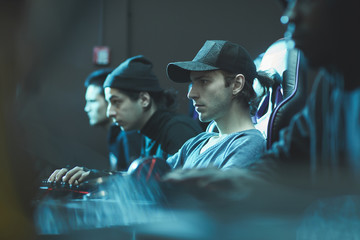 Serious focused young man in cap sitting in row of programmers and working on software in database center