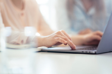 Girls dressed in casual discuss work issues, hands on a laptop