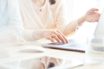 Girls dressed in casual discuss work issues, hands on a laptop