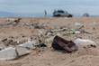 Polluted sand beach full of plastic bottles and other garbage the left by tourists during summer vacation, a car and people on the background. Planet pollution, environmental problem, contamination 