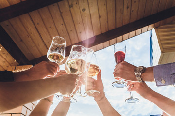 Human hands with glasses of red wine clinking them over served table.