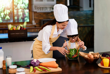 Happy asian family in the kitchen.Mother and son help to make vegetable salad.Mom teaching kid boy cooking healthy salad for dinner.