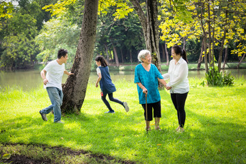 Happy family,asian little child girl or daughter playing touch,tag game,fun,running with father,senior grandmother and mother having smile,laugh in outdoor park,parents enjoy,happy vacation concept