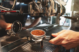 barista holding coffee holder with ground coffee near professional coffee machine close up