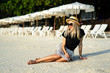 © Artem Markin - A girl in a straw hat sits on the morning beach. Modern girl on vacation