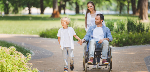 Wall Mural - panoramic shot of beautiful mother rolling wheelchair with disabled father in park near son