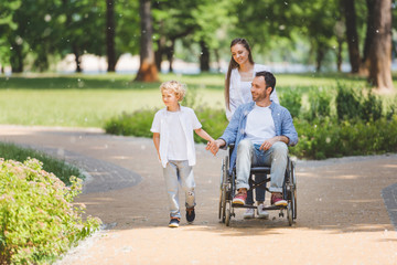 Wall Mural - mother rolling wheelchair with disabled father in park near son