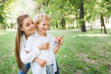 Wall Mural - beautiful mother hugging adorable son pointing with finger at copy space in park