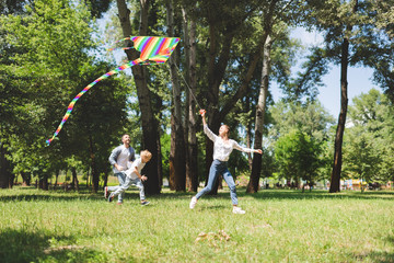 Wall Mural - excited family running and playing with flying kite in park