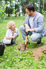 Wall Mural - father and cute son during digging ground with shovel for planting seedling in park