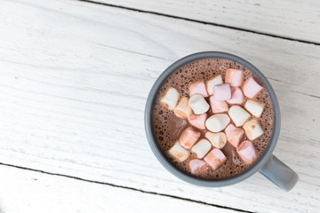 Poster - Hot chocolate with small marshmallows in a blue-grey ceramic mug isolated on white painted wood from above. Space for text.