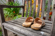 A Pair Of Men's Leather Sandals On A Wooden Seat In A Garden.