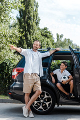 Wall Mural - happy man standing and pointing with finger near son in car