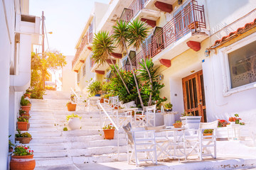 Wall Mural - Outdoor cafe on a traditional greek street with flowers and white architecture, Crete island, Greece