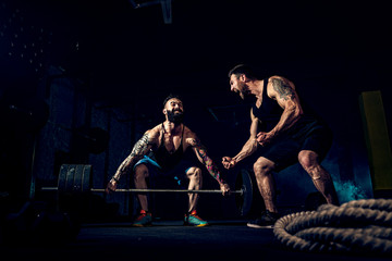 Wall Mural - Two muscular bearded tattoed athletes training, one lift heavy weight bar when other is motivating. Scream. Working hard. Exercise for the muscles of the back