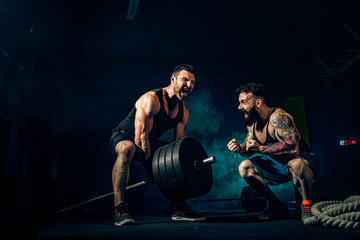 Two muscular bearded tattoed athletes training, one lift heavy weight bar when other is motivating. Scream. Working hard. Exercise for the muscles of the back