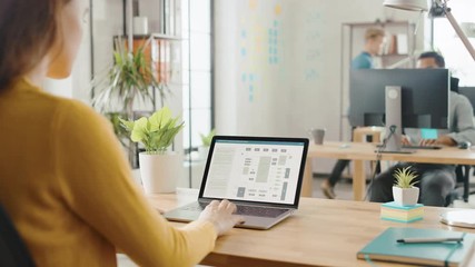 Over the Shoulder: Female Engineer Developer Sitting at Her Desk Using Laptop with Hardware Microchip Design. Office where Diverse Team of Young Professionals Work on Computers