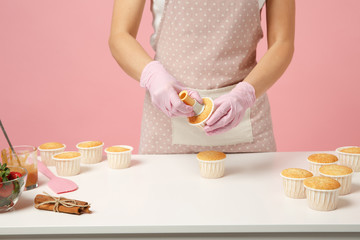 Wall Mural - Close up cropped cute housewife chef cook confectioner or baker in white t-shirt cooking at table isolated on pink pastel background in studio. Cupcake making process. Mock up copy space food concept.