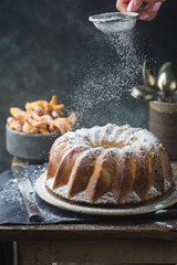 Wall Mural - Rustic Style Apple Bundt Cake Sprinkled with Icing Sugar on old wooden table with woman hands