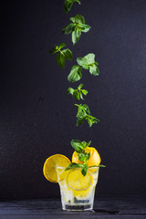 Wall Mural - Lemonade with flying mint and lemon. Summer refreshing drink with lemon on dark background. Infused water with citrus and mint. Summer cocktail in a spray of water. Levitation