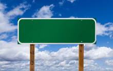 Blank Green Road Sign With Wooden Posts Over Blue Sky And Clouds