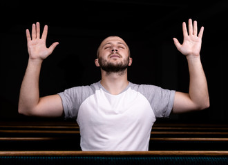 Wall Mural - A Christian man in white shirt is sitting with his hands up and praying with humble heart in the church