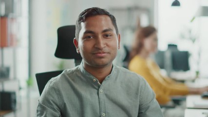 Wall Mural - Portrait of Handsome Professional Indian Man Working at His Desk, Using Personal Computer and Smiling at the Camera. Successful Man Working in Bright Diverse Office