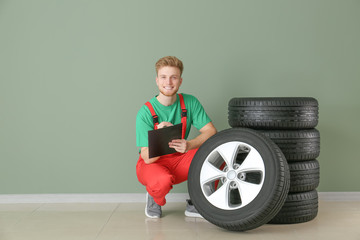 Young male mechanic with car tires near color wall