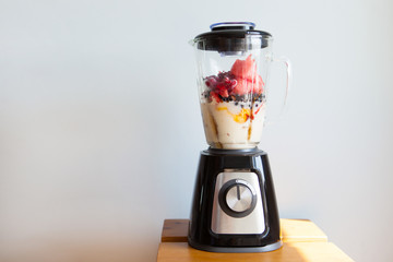 A blender filled with fresh whole fruits for making a smoothie or juice. Healthy eating concept.