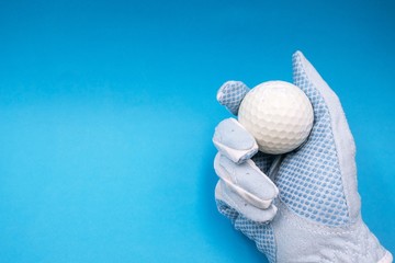 Wall Mural - Hand in blue golf ball is holding white golf ball is on on blue sky background.