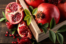 Ripe Tasty Red Pomegranate Fruit With Leaves In A Wooden Box On A Brown Wooden Table. Top View