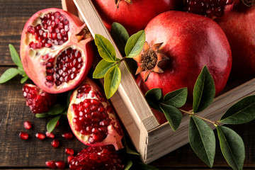 Ripe tasty red pomegranate fruit with leaves in a wooden box on a brown wooden table. top view